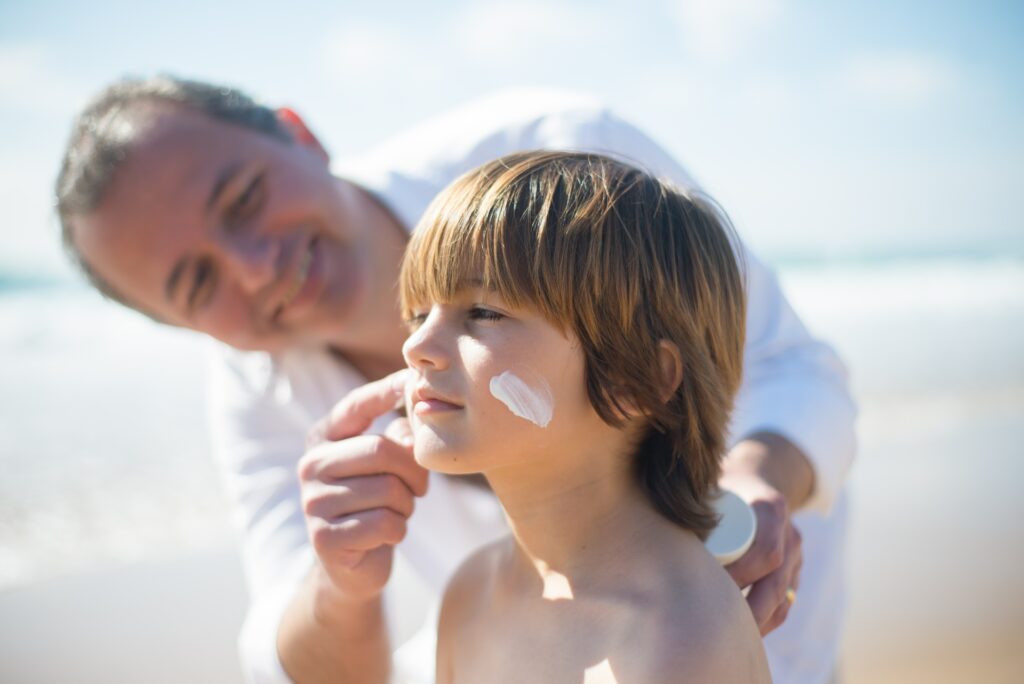 Vater cremt Sohn mit Sonnencreme ein.